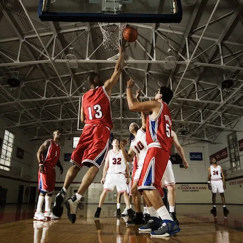 Basketball player in red jersey number 13 shooting over defender in white jersey number 32 under indoor court hoop