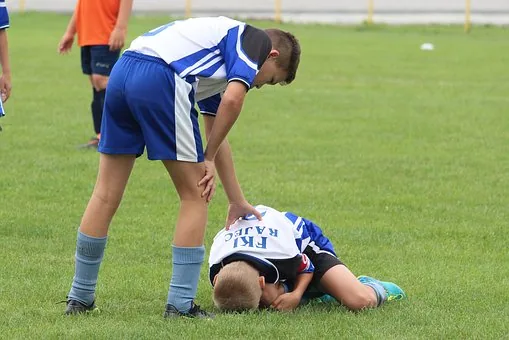 Youth soccer player bending over to assist injured teammate lying on grass during match
