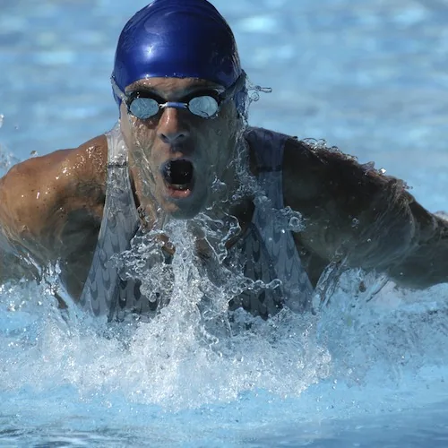 Swimmer performing butterfly stroke in pool wearing blue cap and goggles